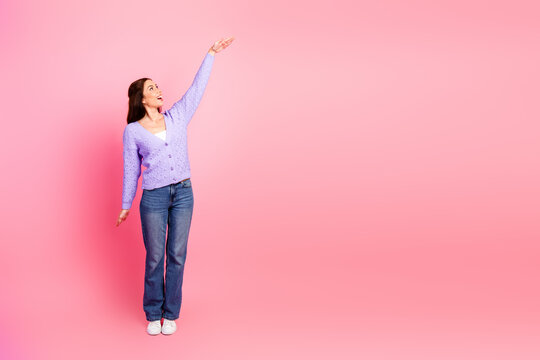 Young chic woman in purple cardigan reaching up against pink background for fashion lifestyle advertising