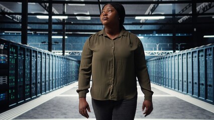 Supervisor in data center overseeing large scale IT equipment to maintain seamless operations. IT expert walking between server room rows, doing network management for increased uptime, camera A