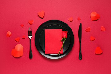 Table setting for Valentine's Day with rose flower, blank paper card and decorative hearts on red...