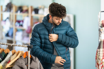 Undetermined young man posing in warm down jacket during shopping in retail outlet