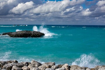 Aqua blue beach with waves crashing on rocks on sunny day