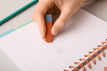 Woman erasing word HELLO from notebook on white background