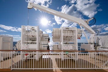 racks containing Inflatable life raft in white round container box on cruise ship outdoors in summer.
