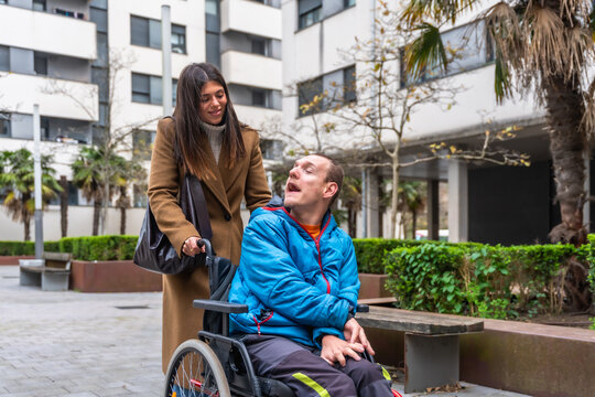 Woman walking with adult man in wheelchair outdoors