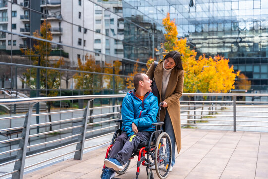 Caregiver pushing adult man in wheelchair in city