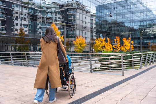 Woman pushing person in wheelchair on urban sidewalk