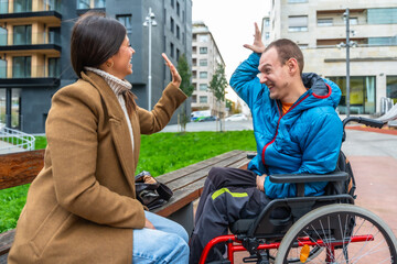 Young woman greeting disabled man in wheelchair with a high five