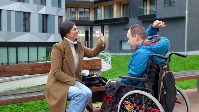 Young man with a physical disability in a wheelchair having an engaging conversation with a female social worker in a city park, showing support, inclusion, and positive communication