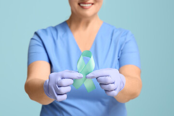 Mature female doctor with teal ribbon on blue background, closeup. Cervical Health Awareness Month