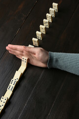 Woman stopping domino effect on black wooden background