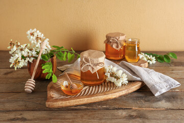 Bowl and jars of sweet honey with acacia flowers on wooden table