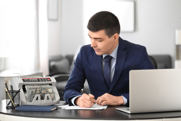 Male bank manager working with cash counting machine in office