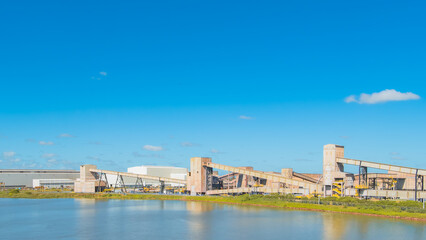 Large industrial complex with conveyor systems located by a lake under a clear blue sky. Professional shot of manufacturing and logistics facility