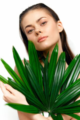 Portrait of a young woman with long hair holding a large green leaf, showcasing natural beauty and serenity in a bright, minimalist setting.