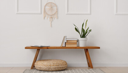 Ottoman and books with houseplant on wooden bench near white wall in room