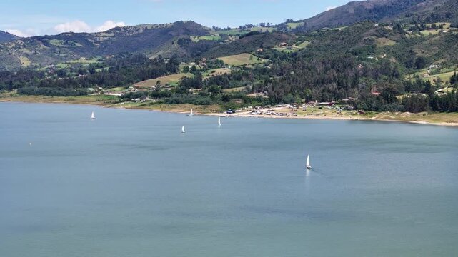 Traveling en el paisaje de la laguna de Tomin&eacute;, rodeado de monta&ntilde;as, con bosques y algunos veleros.