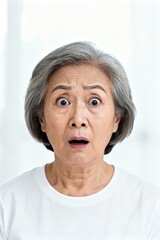 A mature woman expresses extreme surprise with wide eyes and open mouth, framed against white.