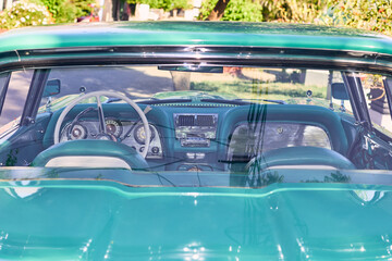 Turquoise vintage car with red lights. Well-maintained and well-painted vehicle, refurbished. Viewed from the front. Parked in an outdoor park at sunset, with natural light.