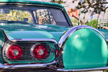 Red taillights of a beautiful turquoise vintage car. Well-maintained and well-painted vehicle, refurbished. Viewed from behind. Parked in an outdoor park at sunset, with natural light.