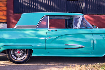 Beautiful antique turquoise car with red lights. Well-maintained and well-painted vehicle, refurbished. Seen from the side. Parked in an outdoor park at sunset, with natural light.