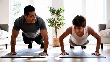 Father and son performing push-ups on exercise mats in a bright room, showcasing strength and determination through synchronized movements and focused expressions - Powered by Adobe