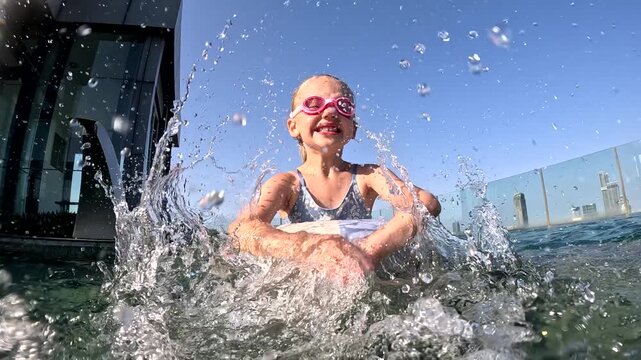 Girl swims and plays in water near modern building during sunny day