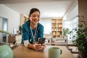 Young female nurse laughing using smartphone at home
