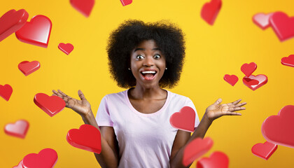 A woman with curly hair smiles widely while shouting in happiness. She is in a yellow studio and has her hands raised, surrounded by floating hearts. This scene captures pure joy and surprise.