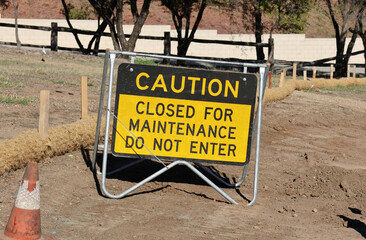 Caution - Closed For Maintenance - Do Not Enter sign mounted on a metal frame and placed on bare dirt
