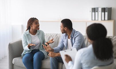 Fototapeta premium Young black couple having conflict during marital therapy with psychologist at office, panorama. Psychotherapist having consultation with African American spouses at clinic. Marriage problems concept