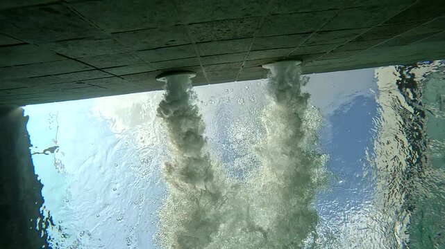 Water flows from multiple outlets under a bridge in a sunny location