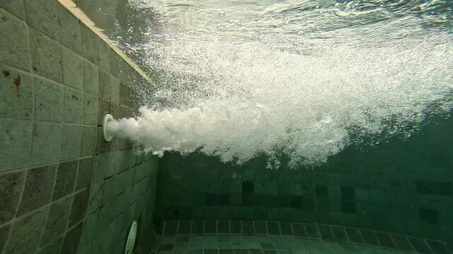 Water bubbles burst from a wall pipe in a pool setting underwater