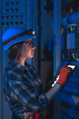 Woman electrician supervises switchboard with tablet on night shift. Remote control.
