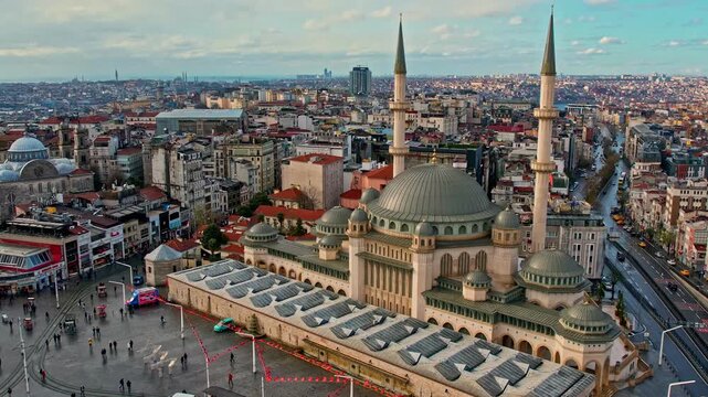 Drone footage of Taksim Square featuring Taksim Mosque, Republic Monument, surrounding streets and the dense Istanbul skyline under bright daylight.