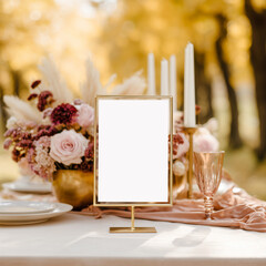 Elegant table setup outdoors in autumn with a table sign mockup surrounded by pastel flowers, candles, and fine tableware
