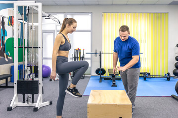 Woman with trainer practices box step up in gym. Box step up.