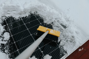 Cleaning snow from solar panel in winter with brush.Close-up view of a solar panel being cleaned from snow using a brush during winter. cold weather conditions, sustainable and eco-friendly power
