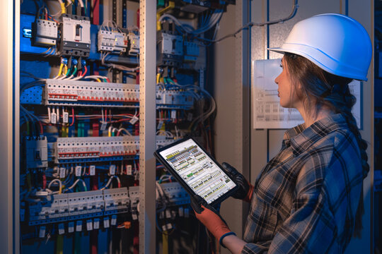 Woman electrician inspects wiring and breakers in cabinet. Switchgear check.