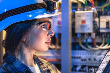 Female electrician wearing safety glasses in control cabinet. Closeup profile. © puhimec