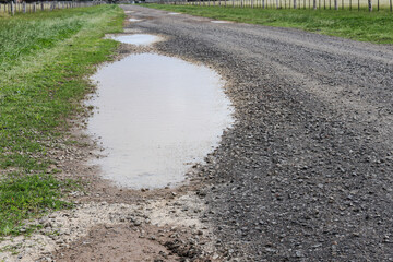 gravel road in the country with pot holes filled with water after rain