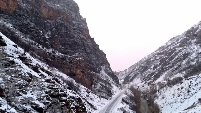A dramatic aerial view of snowy cliff walls, a winter road and rugged canyon slopes in Munzur Valley. Perfect for nature, geography, winter landscapes and cinematic drone footage.