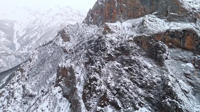 A dramatic aerial view of snowy rocky cliffs and rugged winter mountain terrain in Munzur Valley. Ideal for nature, geography, winter landscapes and cinematic drone footage.