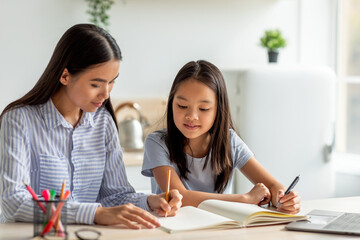 Obraz premium Joint activities and interests concept. Young asian mother and daughter drawing with colourful markers together, sitting at the kitchen table, free space