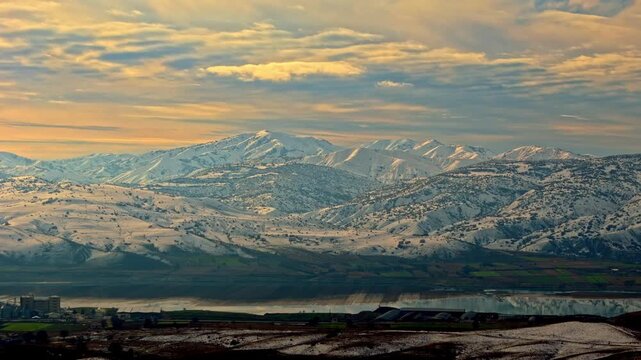 Aerial footage of a reflective river winding through a snowy mountain valley at sunset. Ideal for nature, winter landscapes, geography visuals, travel footage and cinematic drone scenes.
