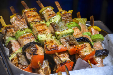Close up of several grilled salmon shish kebabs, interspersed with chunks of zucchini, bell pepper, and eggplant, served on a tray