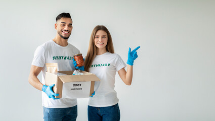 Millennial volunteers wear protective masks and gloves while holding a food donations box. One...