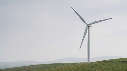 Obraz premium Wind turbine stands tall on a grassy hill, showcasing clean energy on Earth Day in a rural location surrounded by mountains
