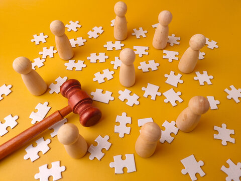 Wooden gavel and wooden figures with scattered puzzle pieces on a yellow background