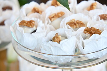 Artisanal walnut sweets in white floral paper liners, elegant wedding dessert table with glass stand, close up of gourmet nut confections for reception, sophisticated party sweets display