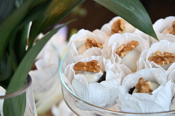 Artisanal walnut sweets in white floral paper liners, elegant wedding dessert table with glass stand, close up of gourmet nut confections for reception, sophisticated party sweets display